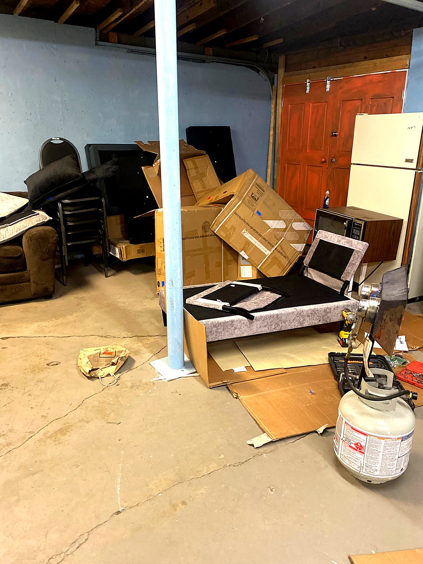 Basement packed with furniture, boxes, and an old refrigerator before removal